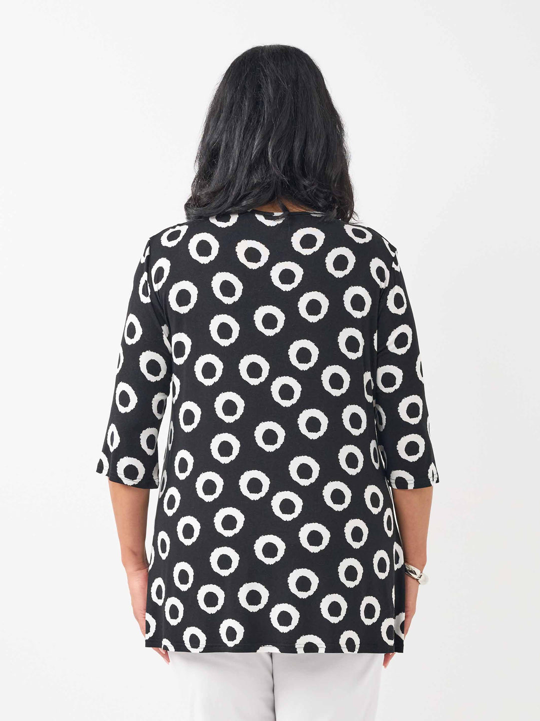 A woman viewed from the back wearing a black three-quarter sleeve top with a white circular dot pattern, paired with white pants