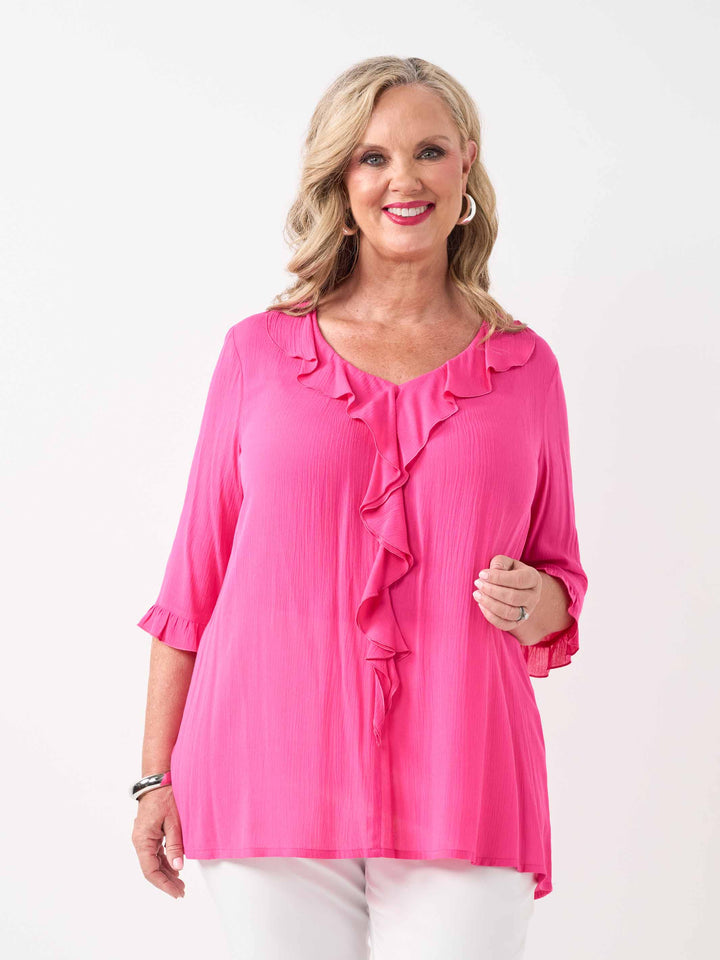 model wearing a bright pink ruffled blouse with three-quarter sleeves and white pants