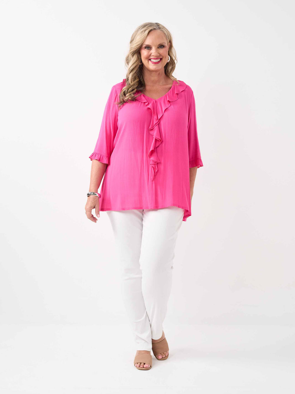 model wearing a bright pink ruffled blouse with three-quarter sleeves and white pants