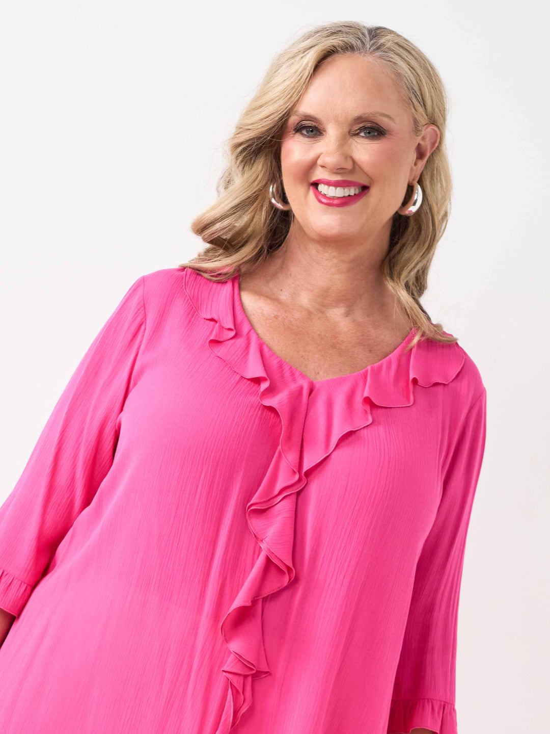 detail view of model wearing a bright pink ruffled blouse with three-quarter sleeves