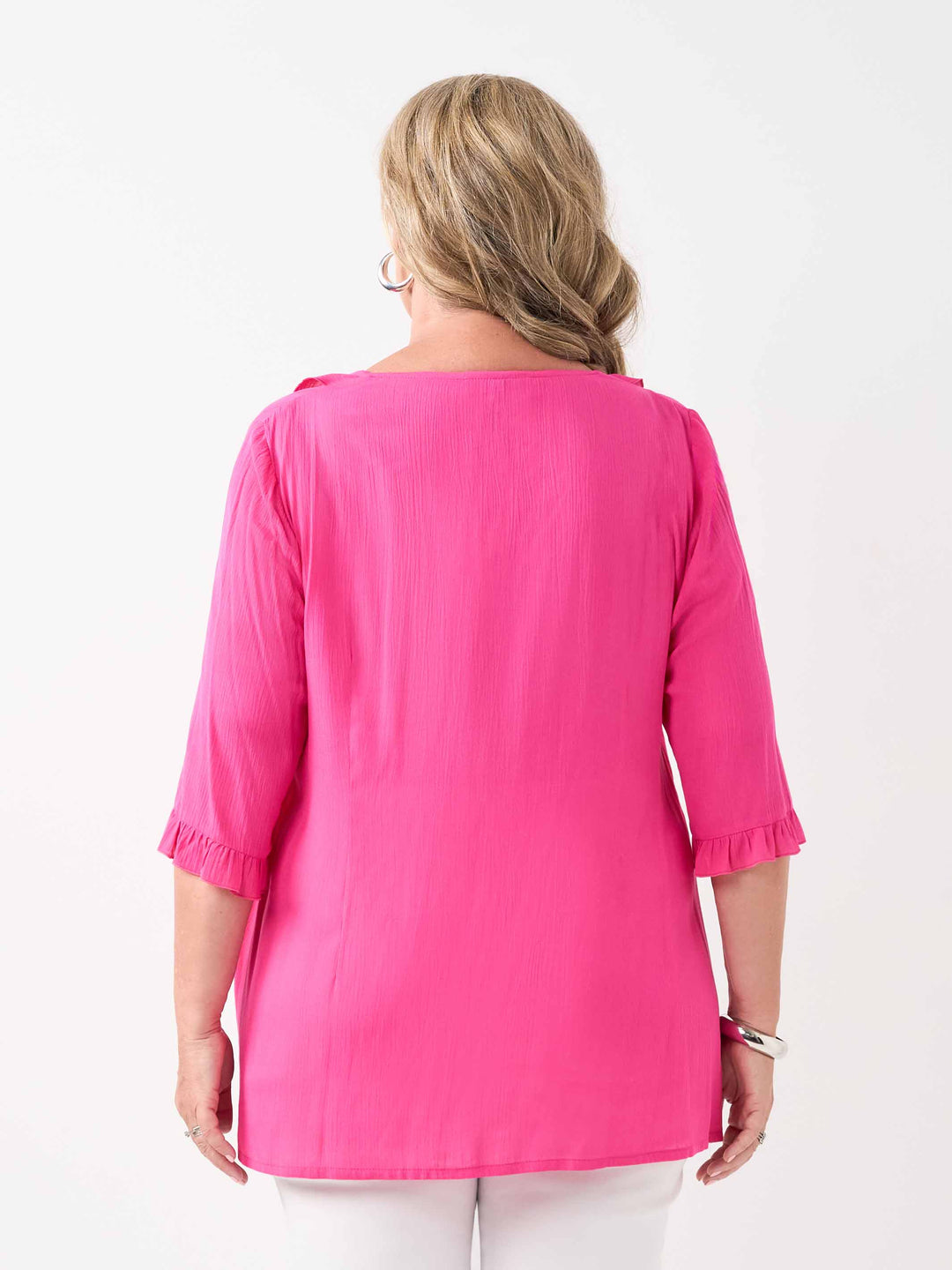 back view of model wearing a bright pink ruffled blouse with three-quarter sleeves and white pants