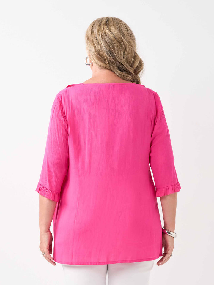back view of model wearing a bright pink ruffled blouse with three-quarter sleeves and white pants