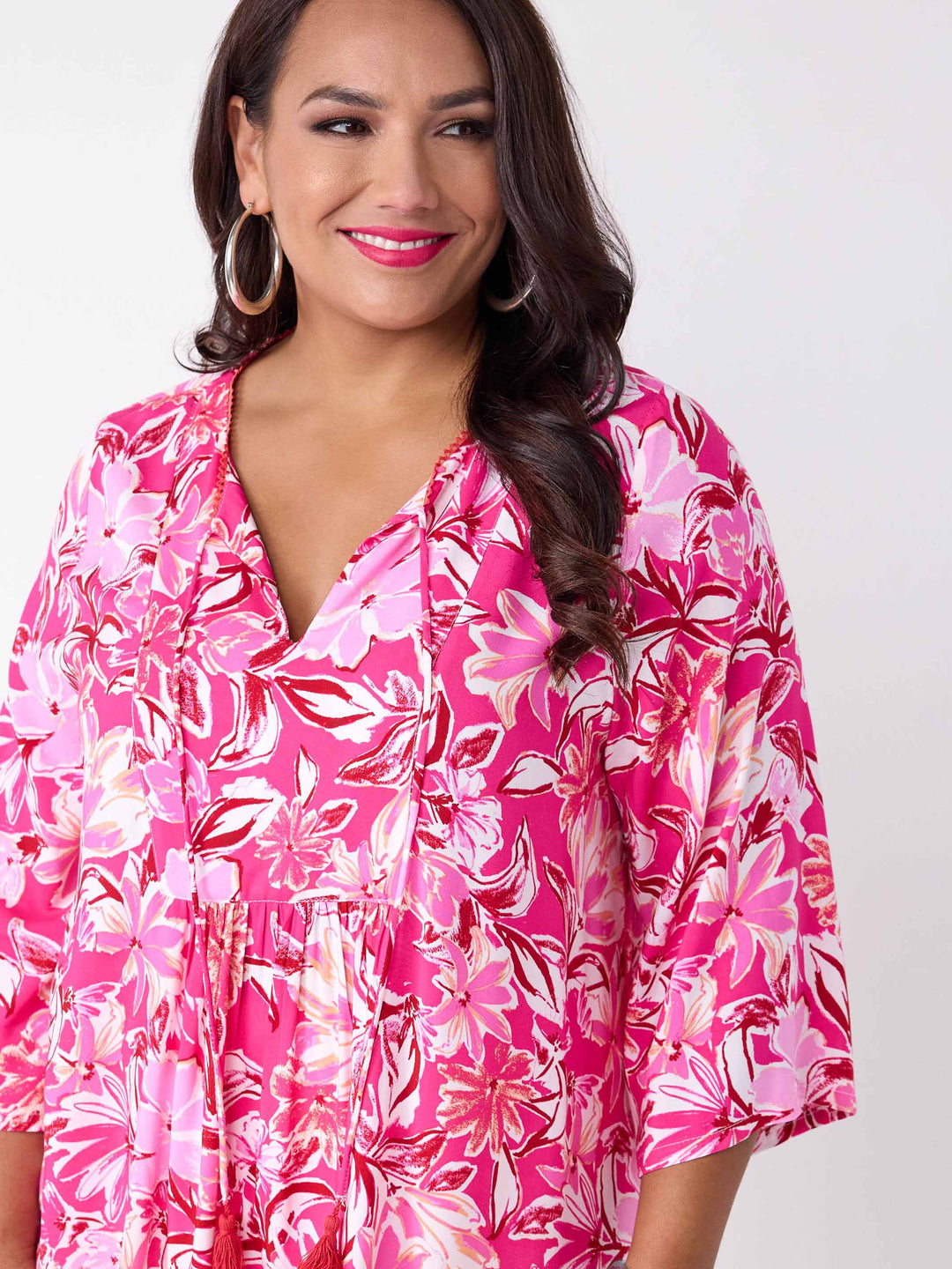A woman wearing a v-neck top with tie neck detail in pretty bright pink floral print