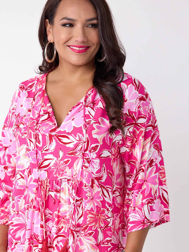 A woman wearing a v-neck top with tie neck detail in pretty bright pink floral print