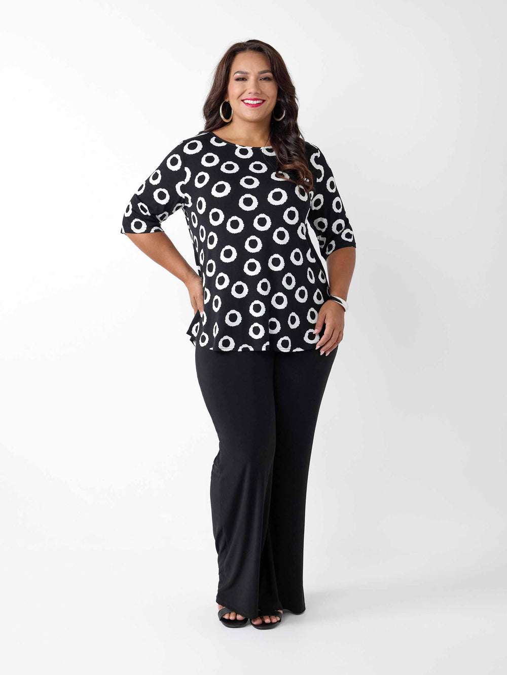 A woman wearing a black short-sleeve top with a white circular dot pattern, paired with black pants