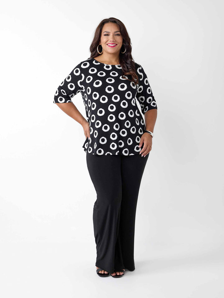 A woman wearing a black short-sleeve top with a white circular dot pattern, paired with black pants