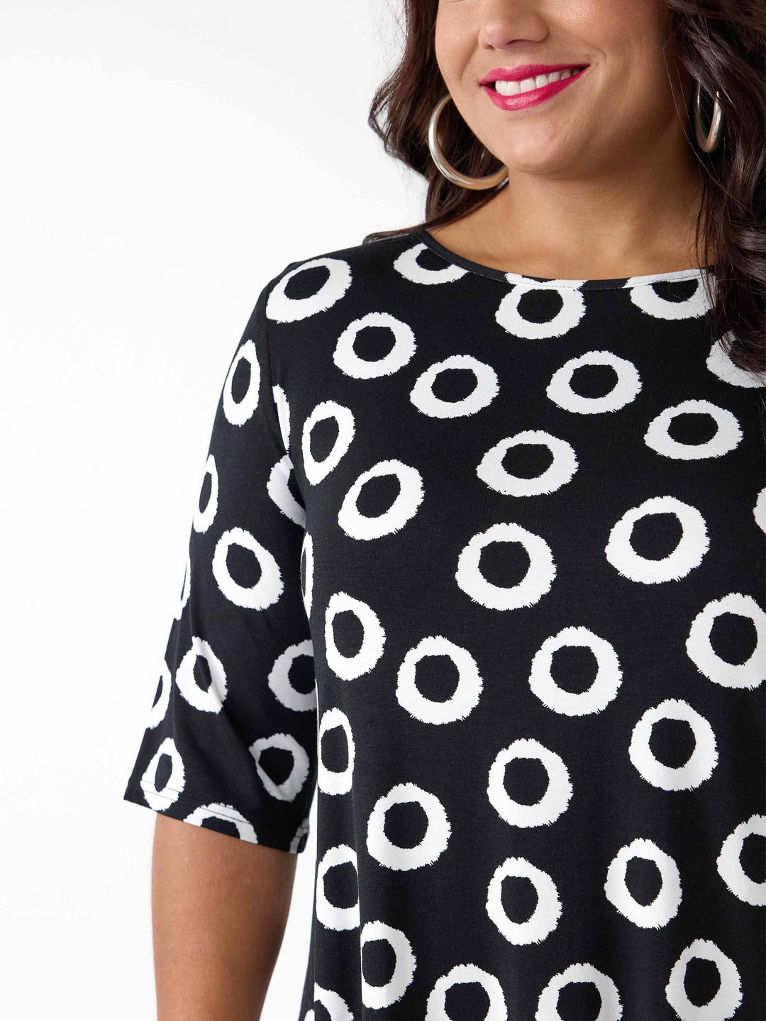 A close-up of a woman wearing a black short-sleeve top with a white circular brushstroke pattern
