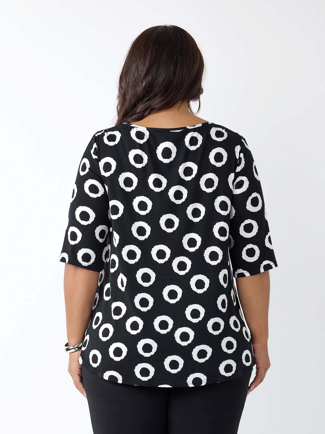 A woman viewed from the back wearing a black short-sleeve top with a white circular dot pattern, paired with black pants