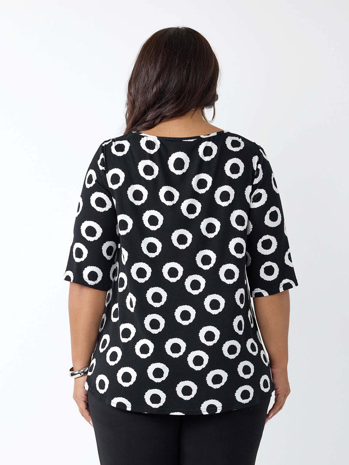 A woman viewed from the back wearing a black short-sleeve top with a white circular dot pattern, paired with black pants