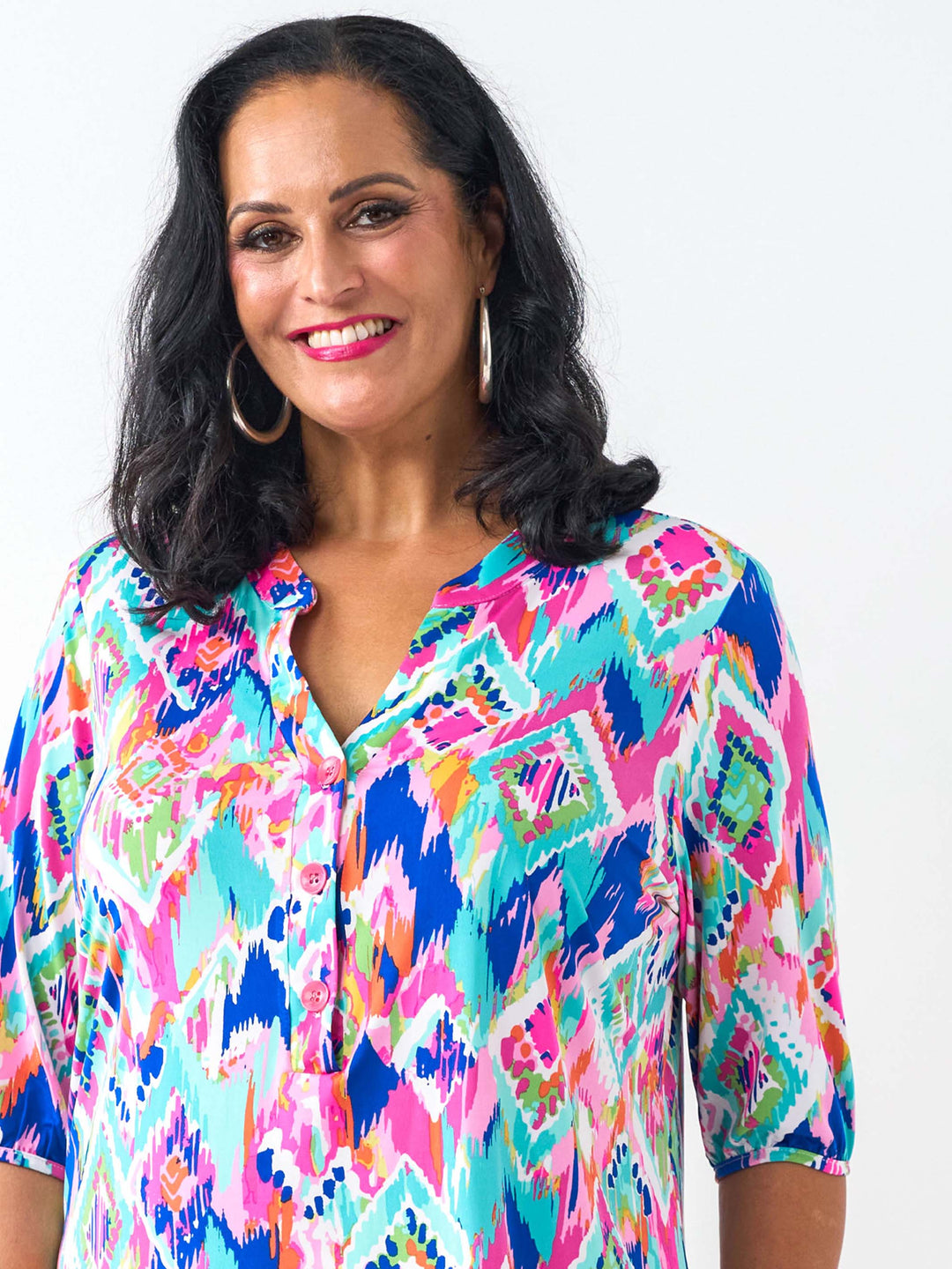 A smiling woman wearing a vibrant, multicoloured geometric patterned blouse with pink, blue, teal, and orange tones