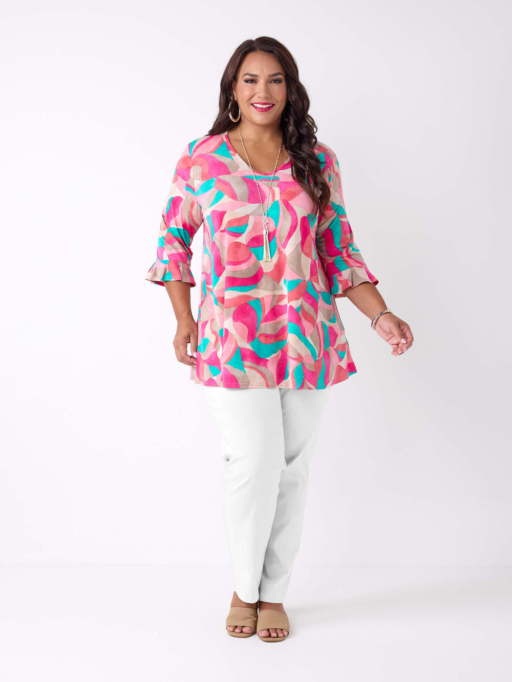 A woman wearing a pink, teal, and beige abstract patterned top top with three-quarter ruffled sleeves, paired with white pants
