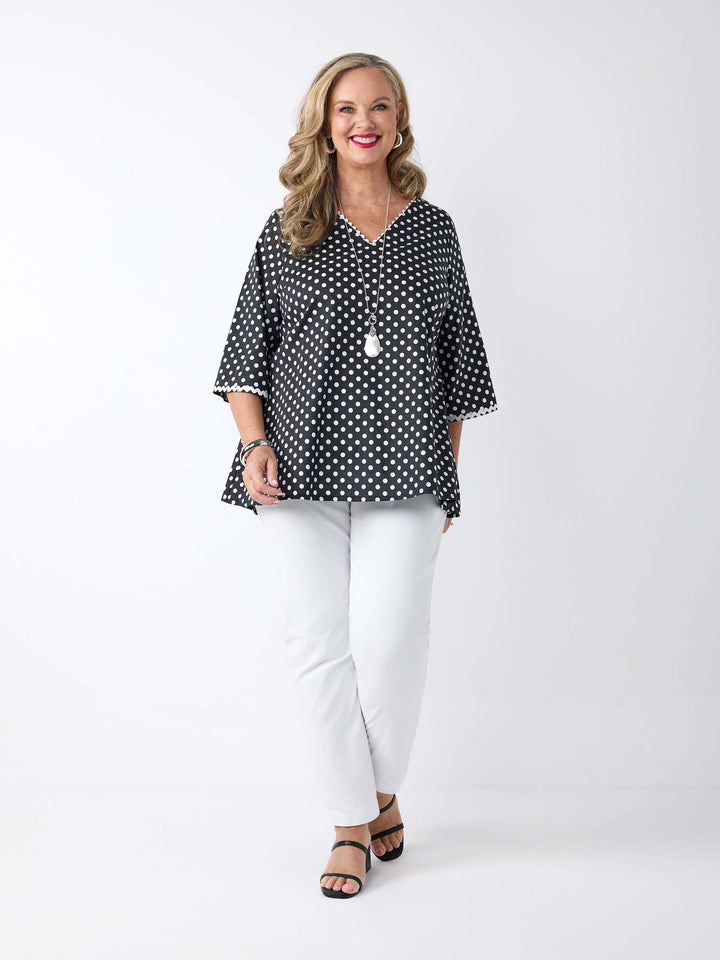 A woman wearing a black and white polka dot v-neck top with ric-rac lace detail around the neckline and sleeves 