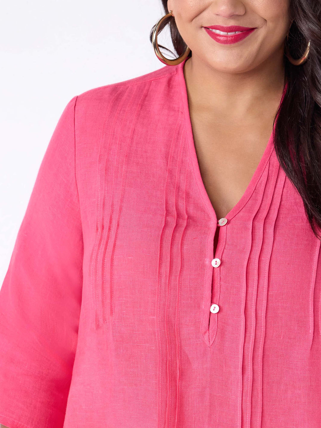 A woman wearing a bright pink linen three-quarter sleeve blouse with a pleated front and button placket