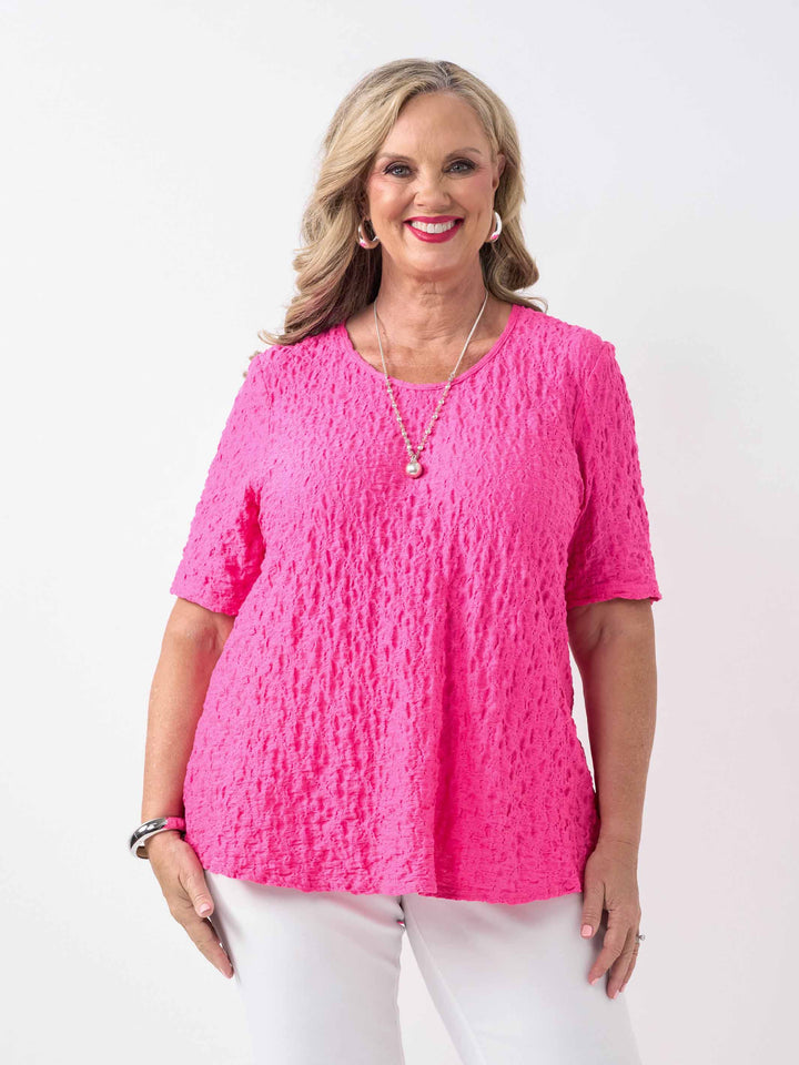 A woman wearing a bright pink textured short-sleeve top and white pants