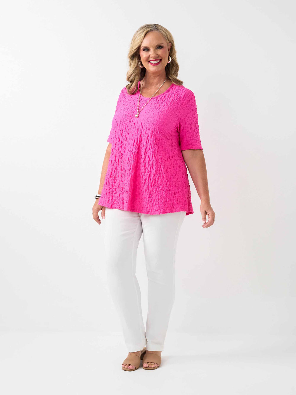 A woman wearing a bright pink textured short-sleeve top and white pants