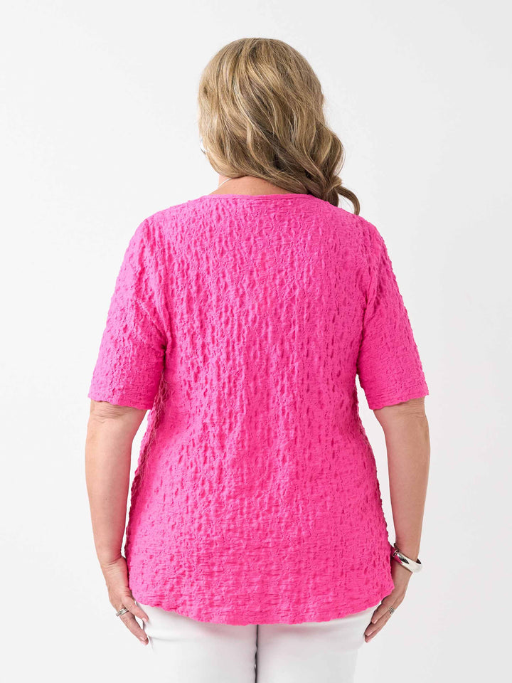 A woman viewed from the back wearing a bright pink textured short-sleeve top and white pants