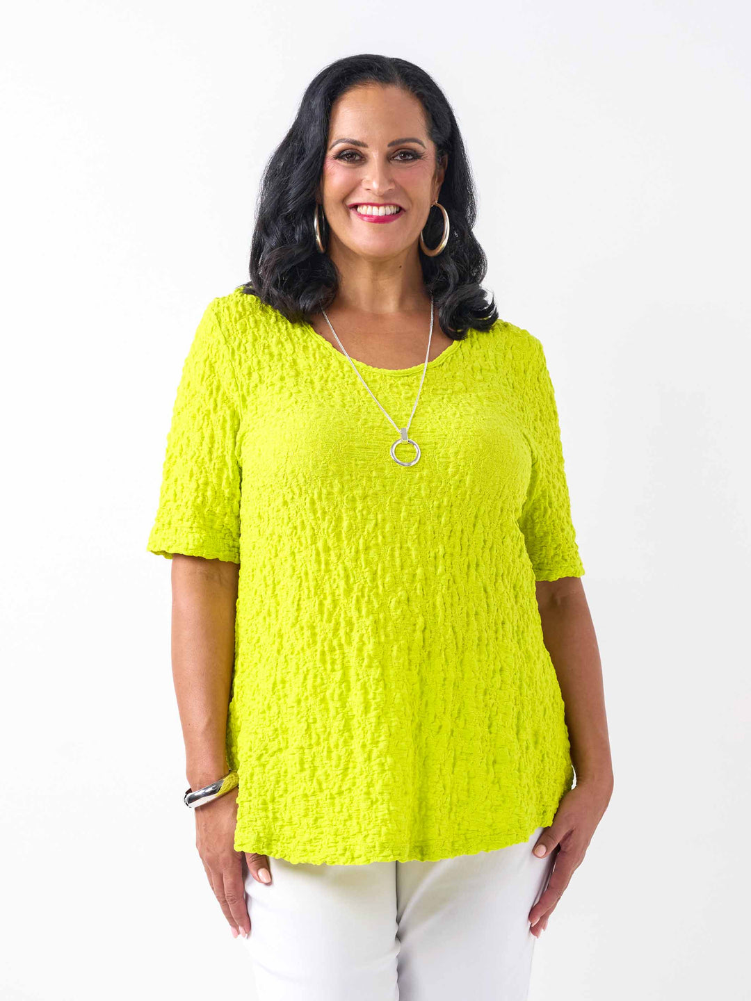 A woman wearing a fresh bright lime yellow-green textured short-sleeve top and white pants.