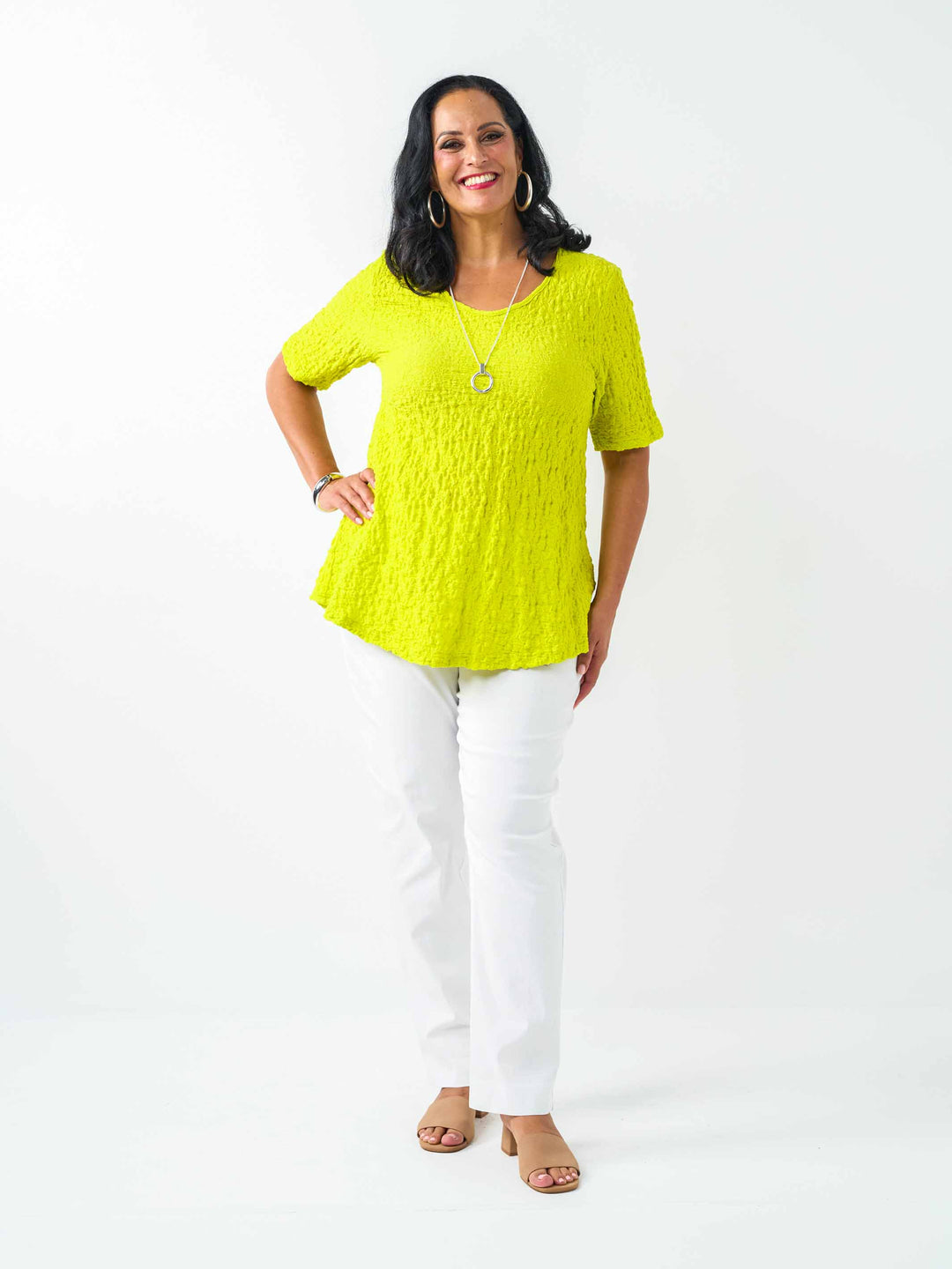 A woman wearing a fresh bright lime yellow-green textured short-sleeve top and white pants.