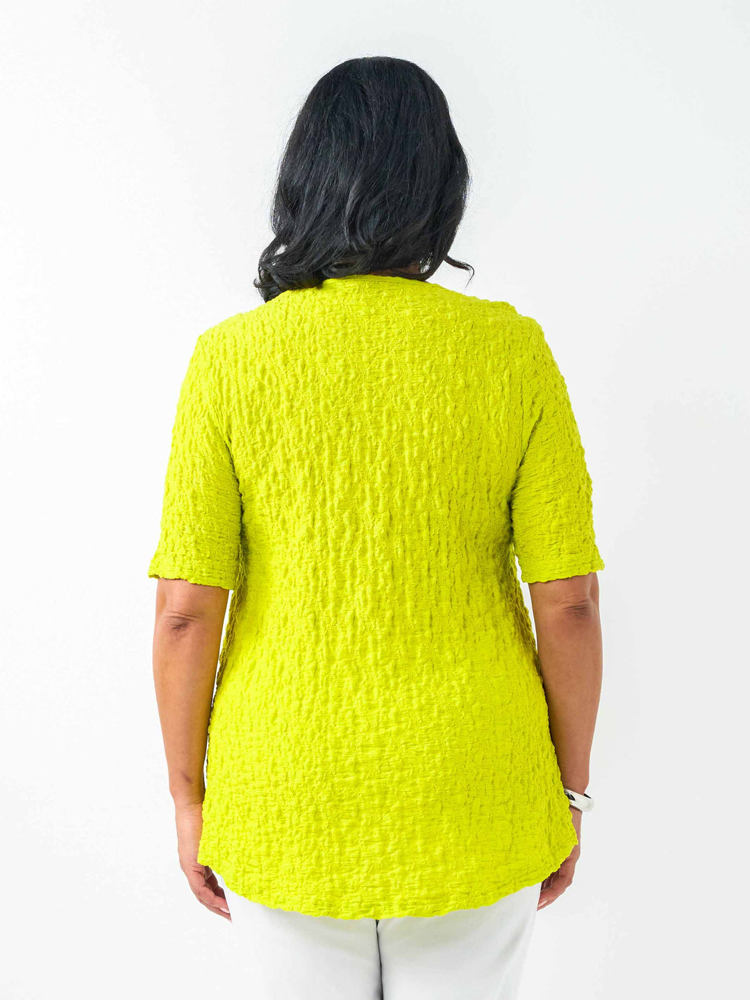 A woman wearing a fresh bright lime yellow-green textured short-sleeve top and white pants.