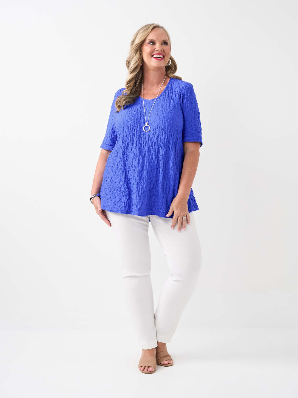 A woman wearing a bright blue textured short-sleeve top and white pants