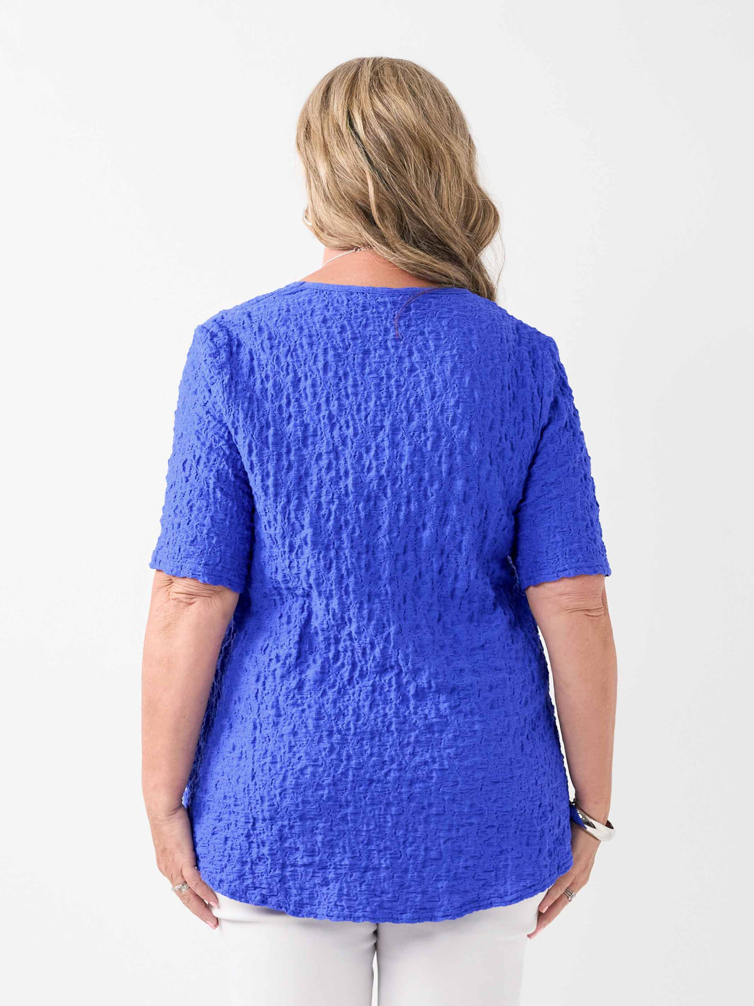 A woman wearing a bright blue textured short-sleeve top and white pants