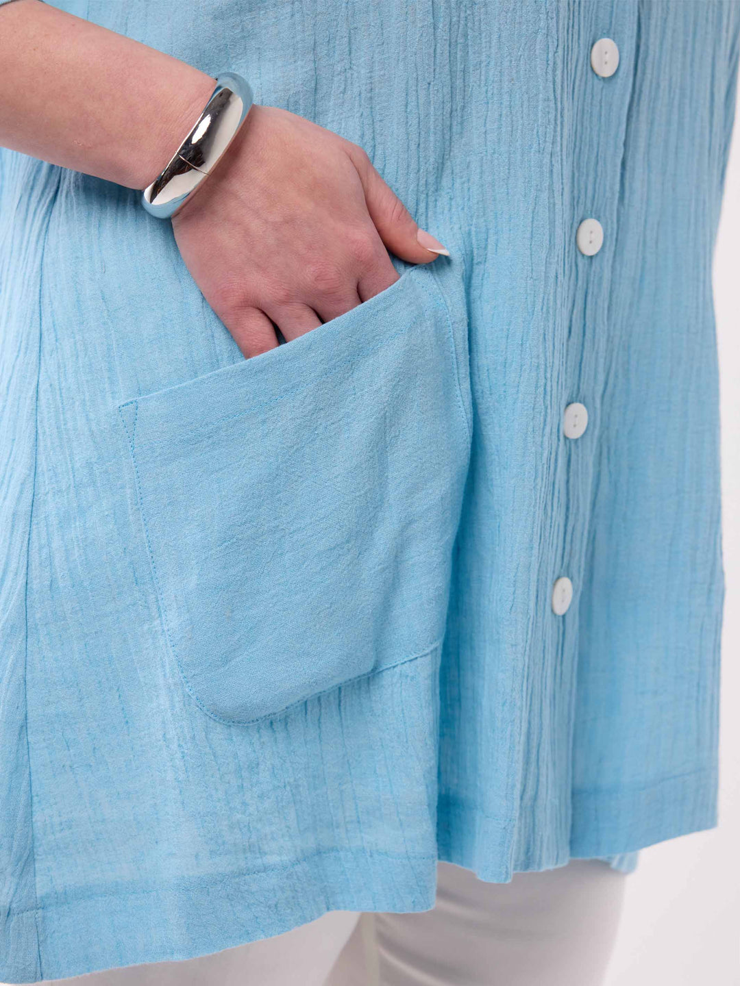 Close-up of a person wearing a light blue crinkled linen shirt with a front pocket and white buttons, showing a hand in the pocket