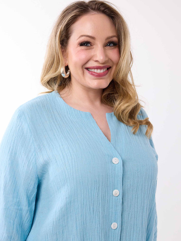 A woman wearing a light blue crinkled button-front top with a split neckline