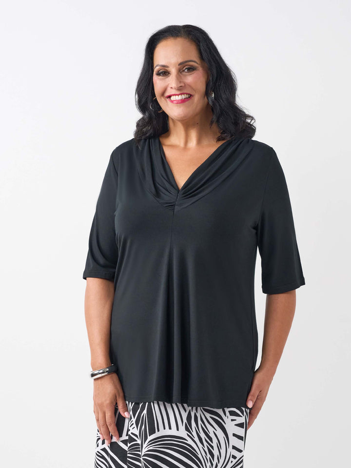 A woman wearing a black short-sleeve top with a draped cowl neckline, paired with black and white tropical palm patterned skirt