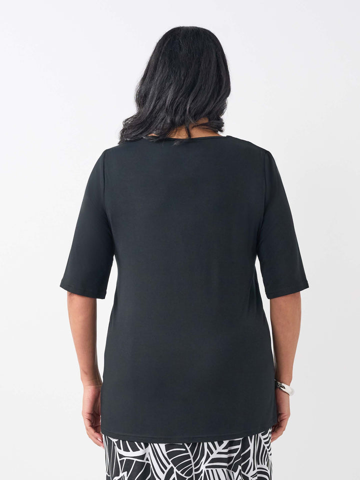 A woman viewed from the back wearing a black short-sleeve top and a black-and-white patterned skirtbackground.