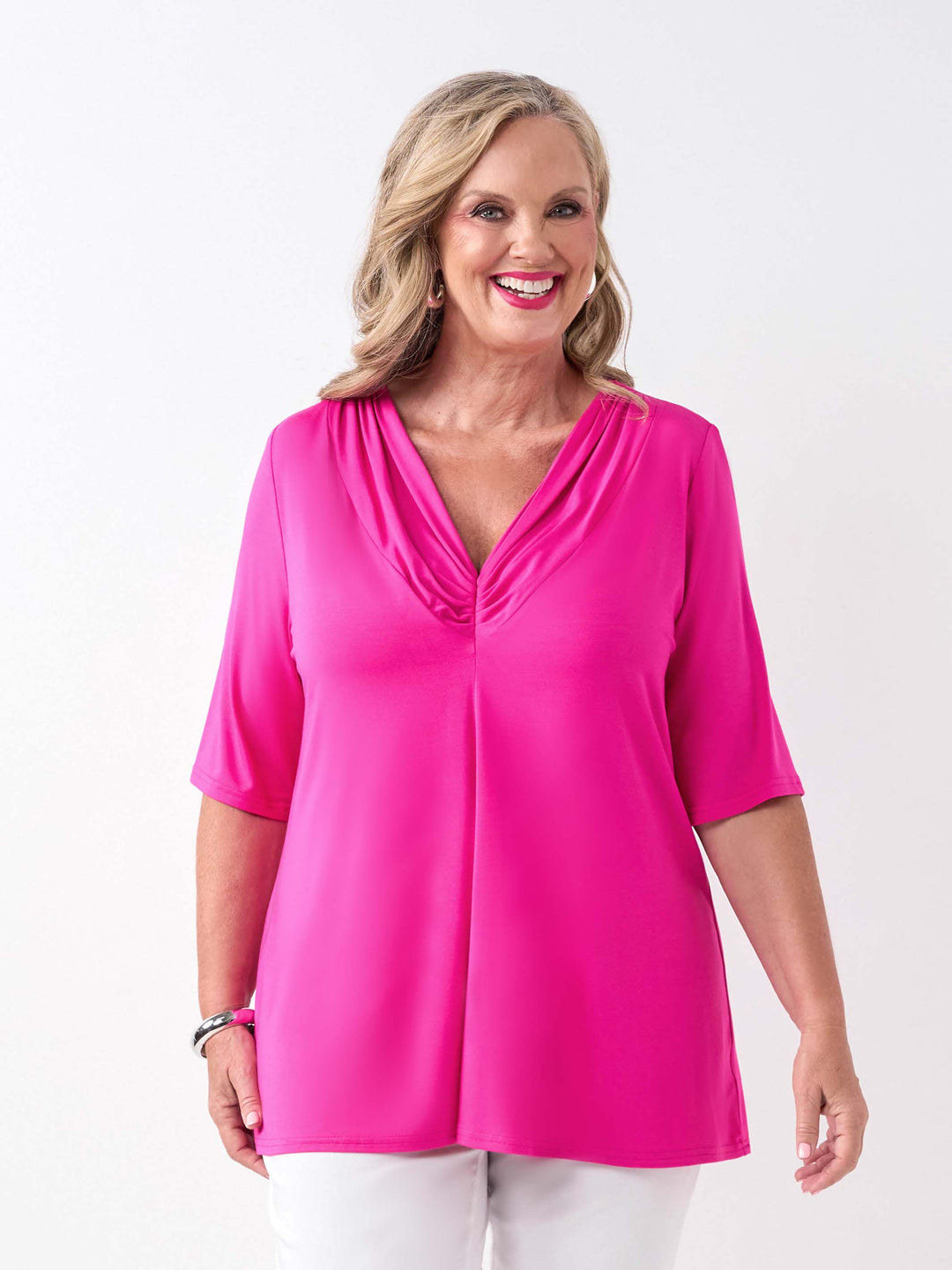 A woman wearing a bright pink short-sleeve top with a gathered V-neckline, paired with white pants