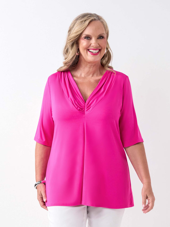 A woman wearing a bright pink short-sleeve top with a gathered V-neckline, paired with white pants