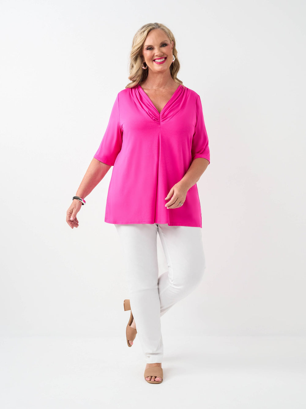 A woman wearing a bright pink short-sleeve V-neck top with white pants