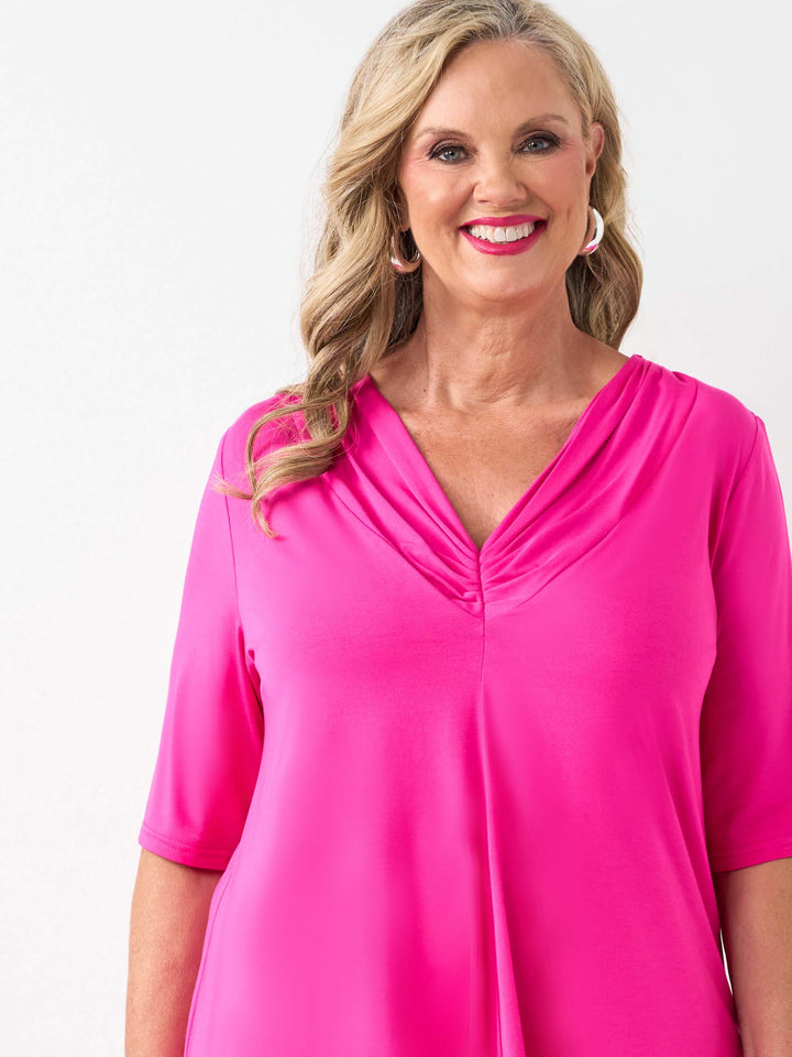 A woman wearing a bright pink short-sleeve top with a gathered V-neckline, paired with white pants