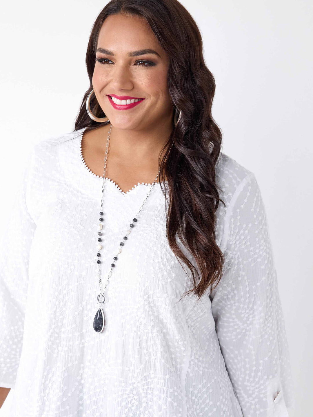 detail view of model wearing a white three-quarter sleeves top with a textured, dotted pattern