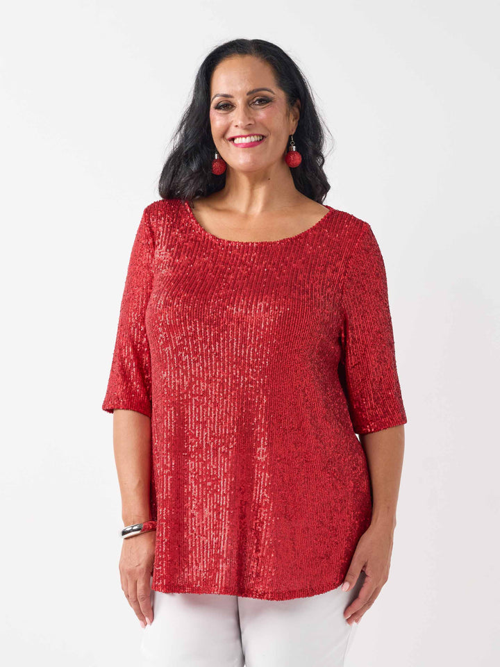 A woman wearing a red sequined short-sleeve top with a scoop neckline, paired with white pants