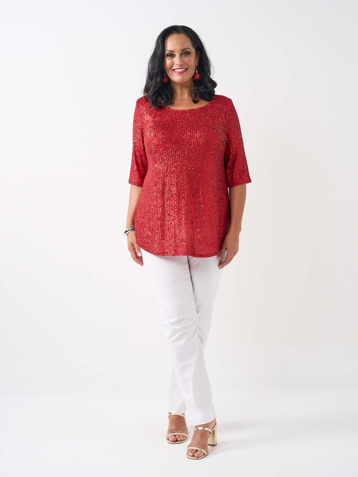 A woman wearing a red sequined short-sleeve top with a scoop neckline, paired with white pants