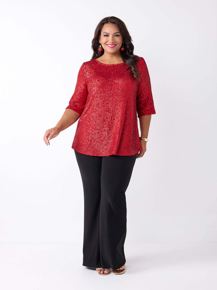 A woman wearing a red sequined short-sleeve top with a scoop neckline, paired with black wide leg palazzo pants