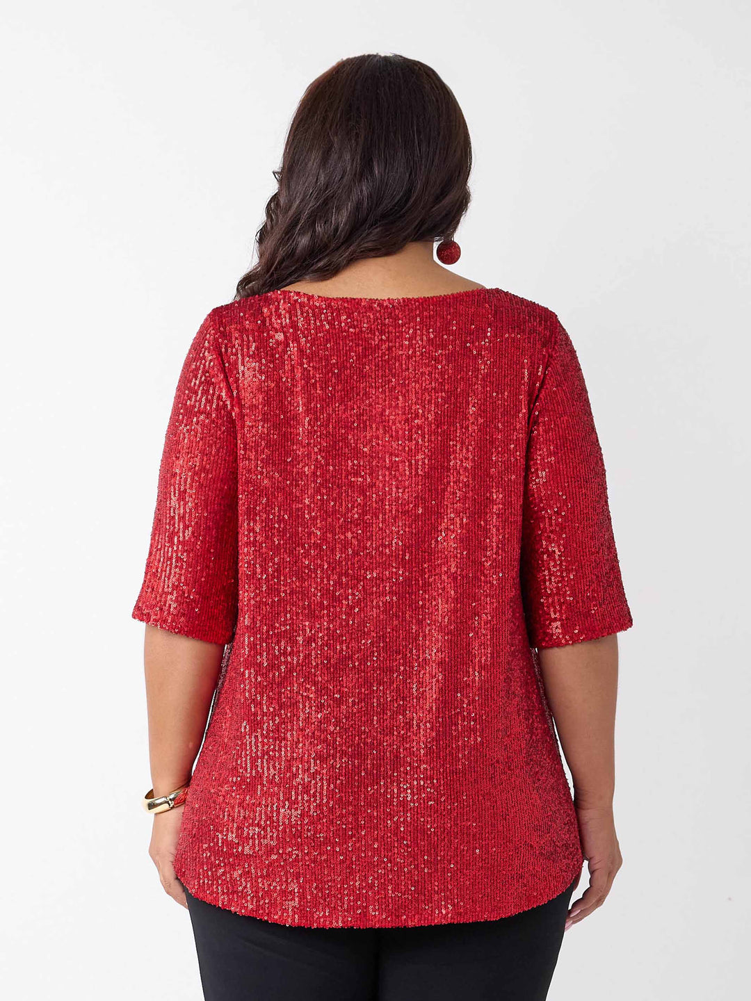A woman viewed from the back wearing a red sequined top with three-quarter sleeves and black pants