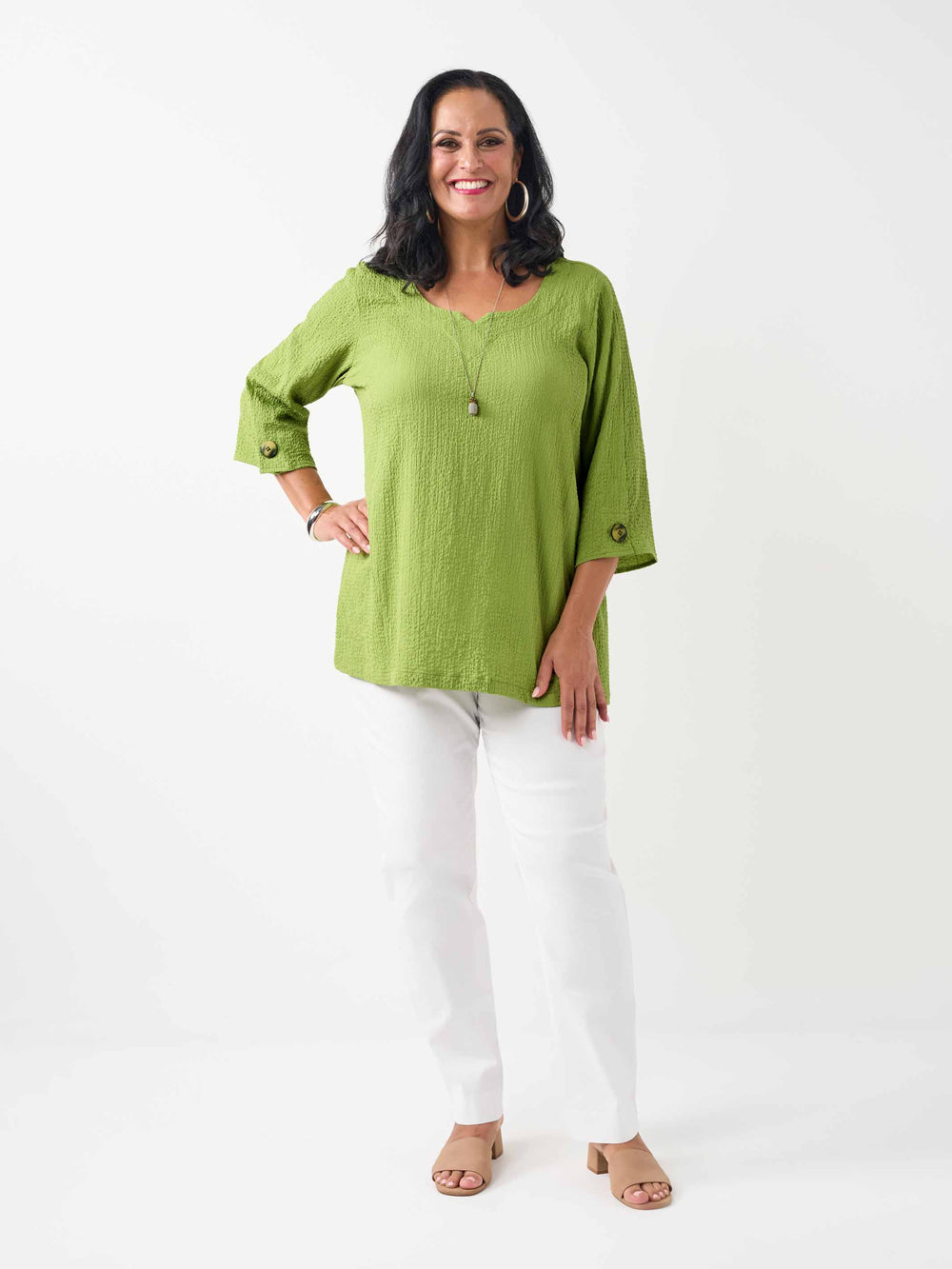 model wearing a lime green textured three-quarter sleeve top with decorative buttons on the cuffs, paired with white pants 