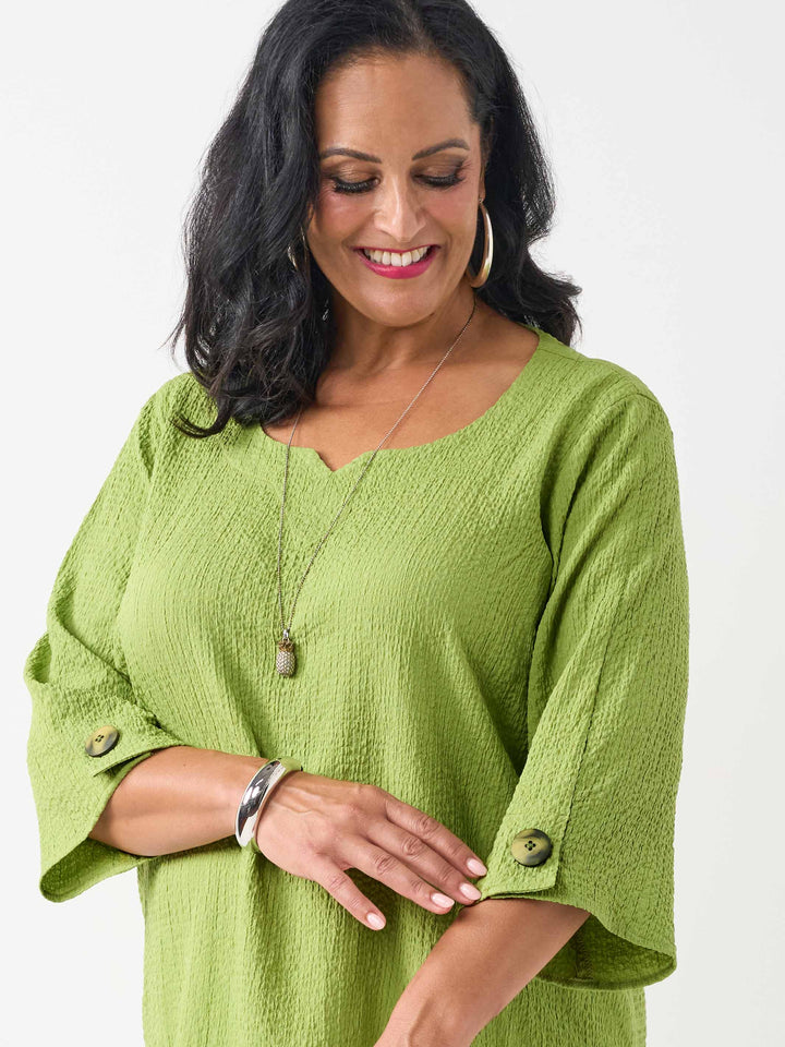 detail view of model wearing a lime green textured three-quarter sleeve top with decorative buttons on the cuffs