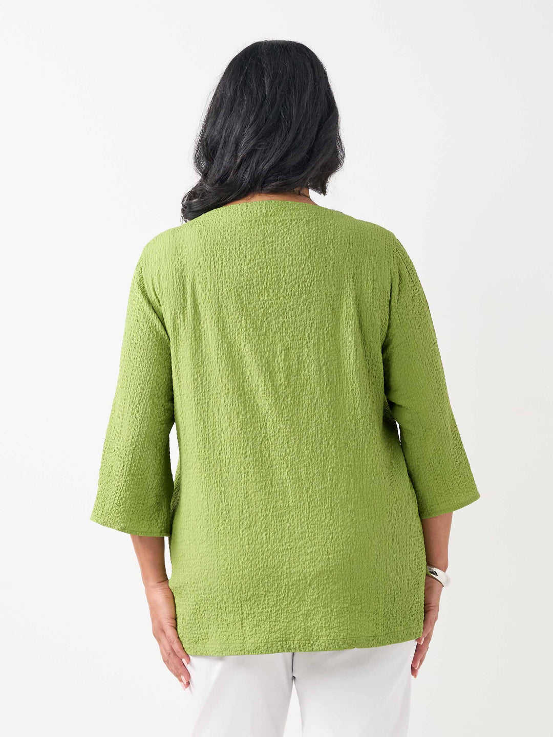 back view of model wearing a lime green textured three-quarter sleeve top with decorative buttons on the cuffs