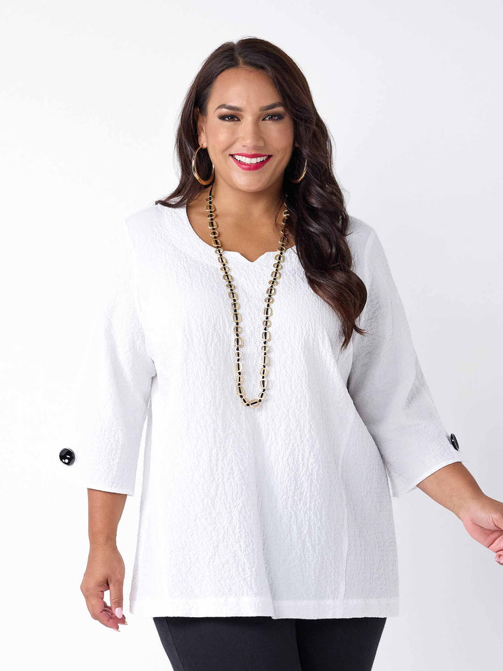 model wearing a white textured three-quarter sleeve top with black buttons on the cuffs