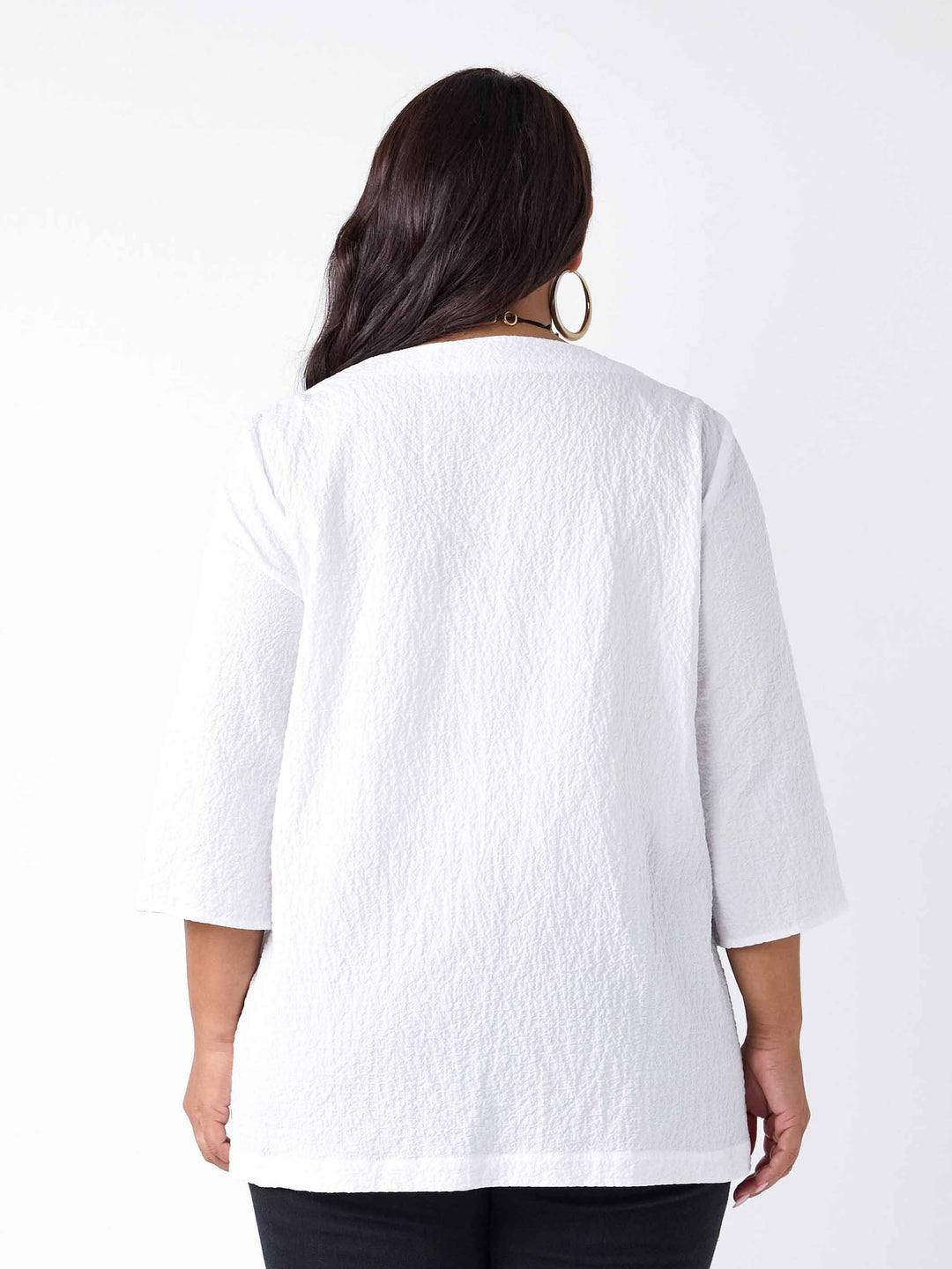 back view of model wearing a white textured three-quarter sleeve top with black buttons on the cuffs