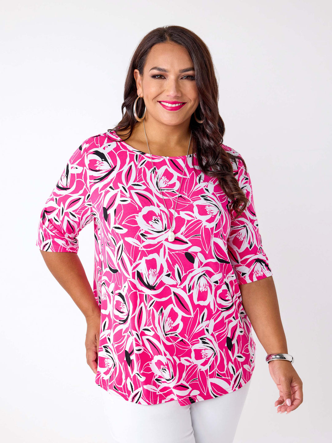 A woman wearing a bright pink three-quarter sleeve top with a bold floral print pattern, paired with white pants