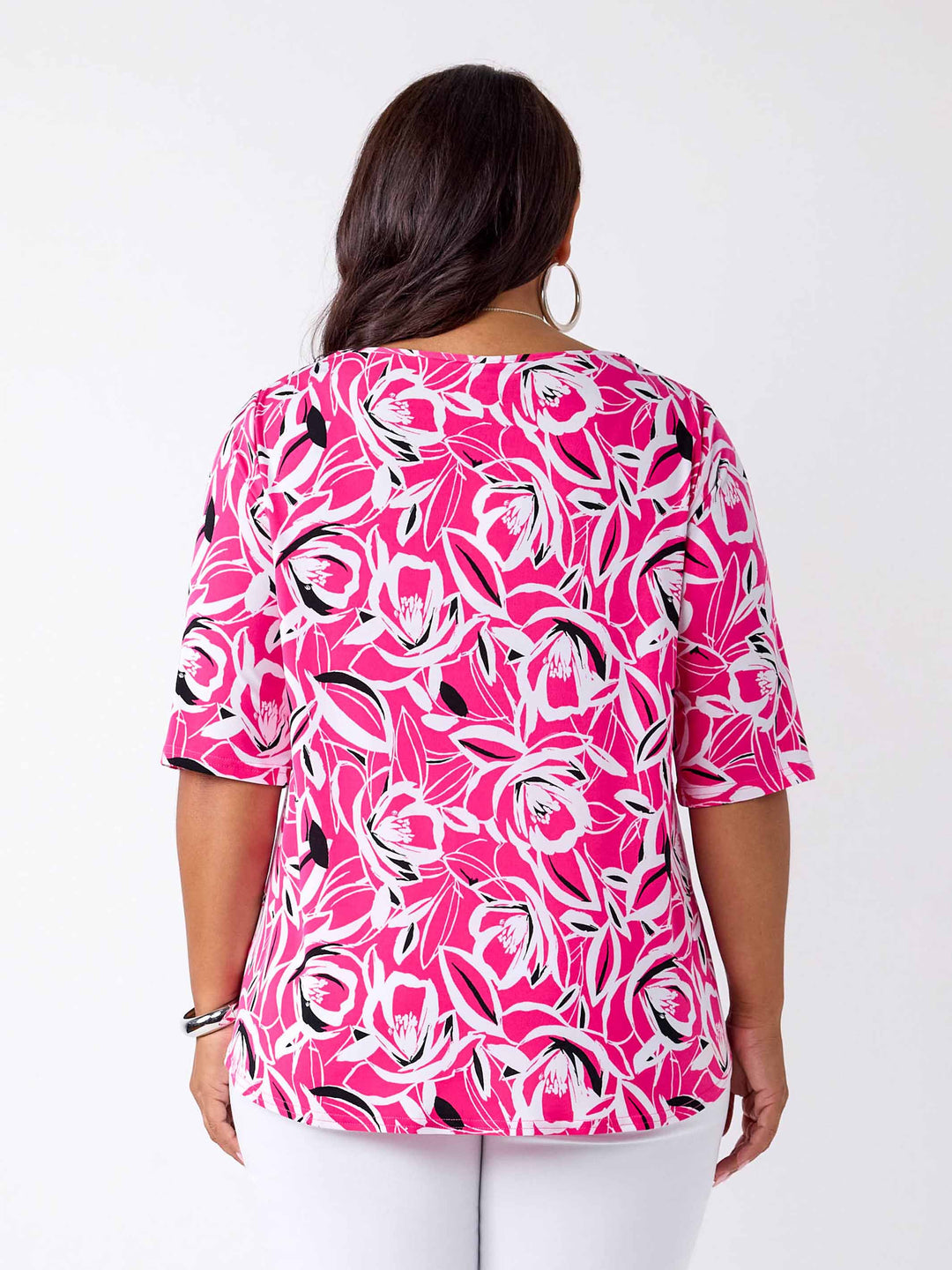 back view of a woman wearing a bright pink three-quarter sleeve top with a bold floral print pattern, paired with white pants
