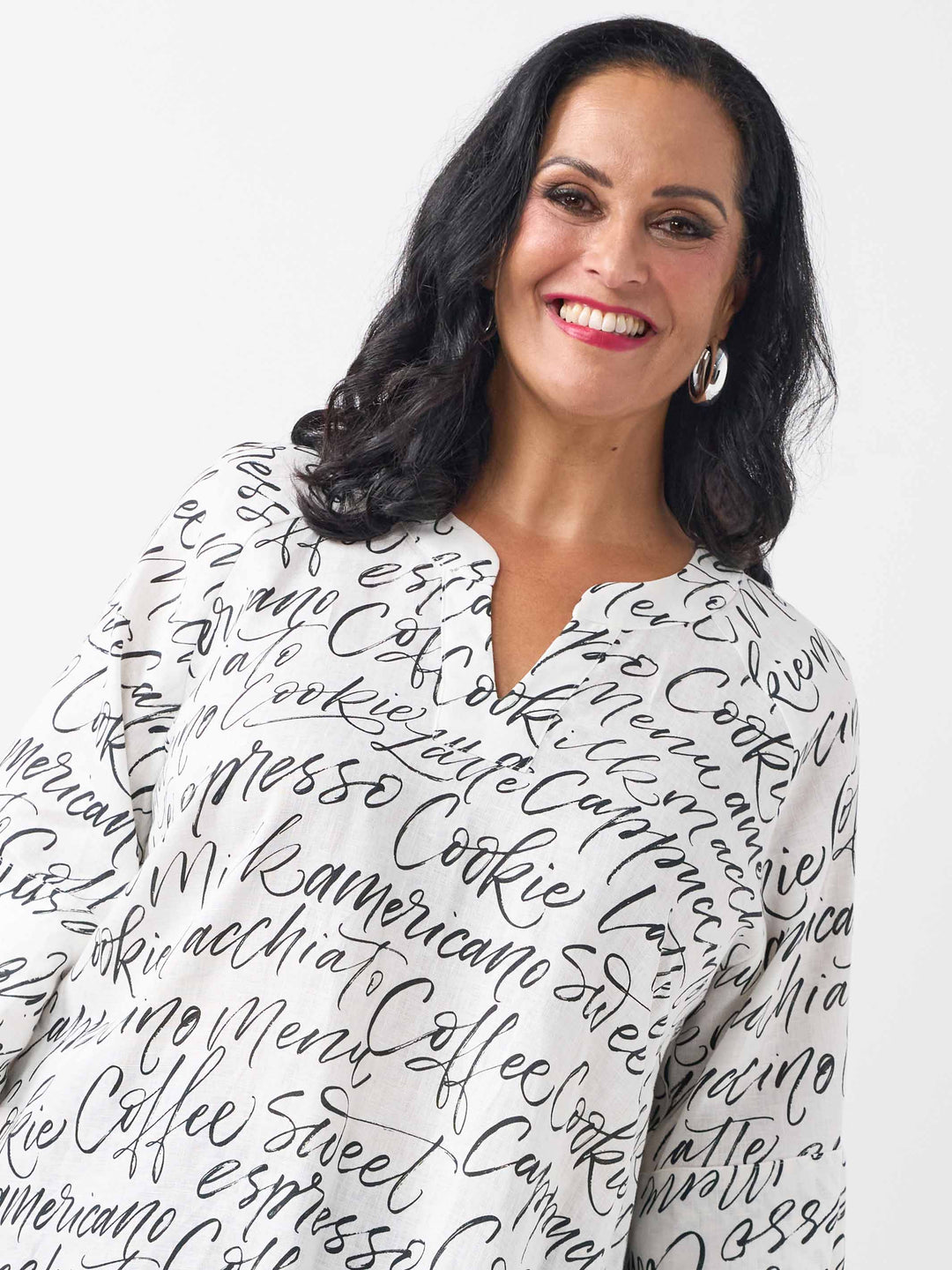 A woman wearing a white three-quarter sleeve top with an all-over black script coffee-themed print, paired with black pant