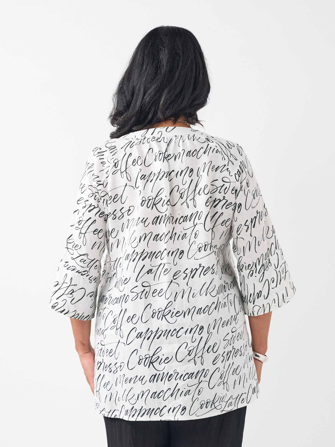 A woman wearing a white three-quarter sleeve top with an all-over black script coffee-themed print, paired with black pant