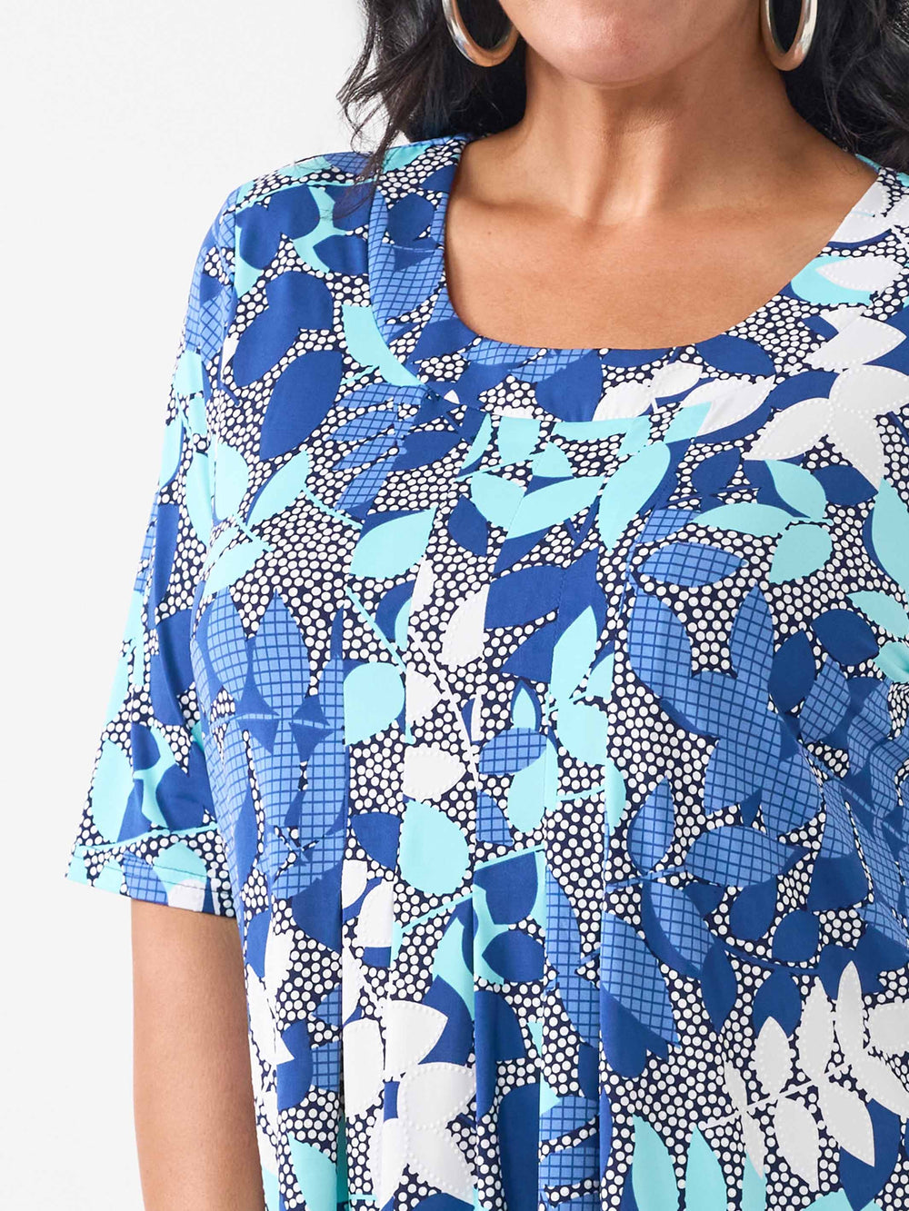 a detail view of woman wearing a short-sleeve top in blue shade with textured white fern detail.