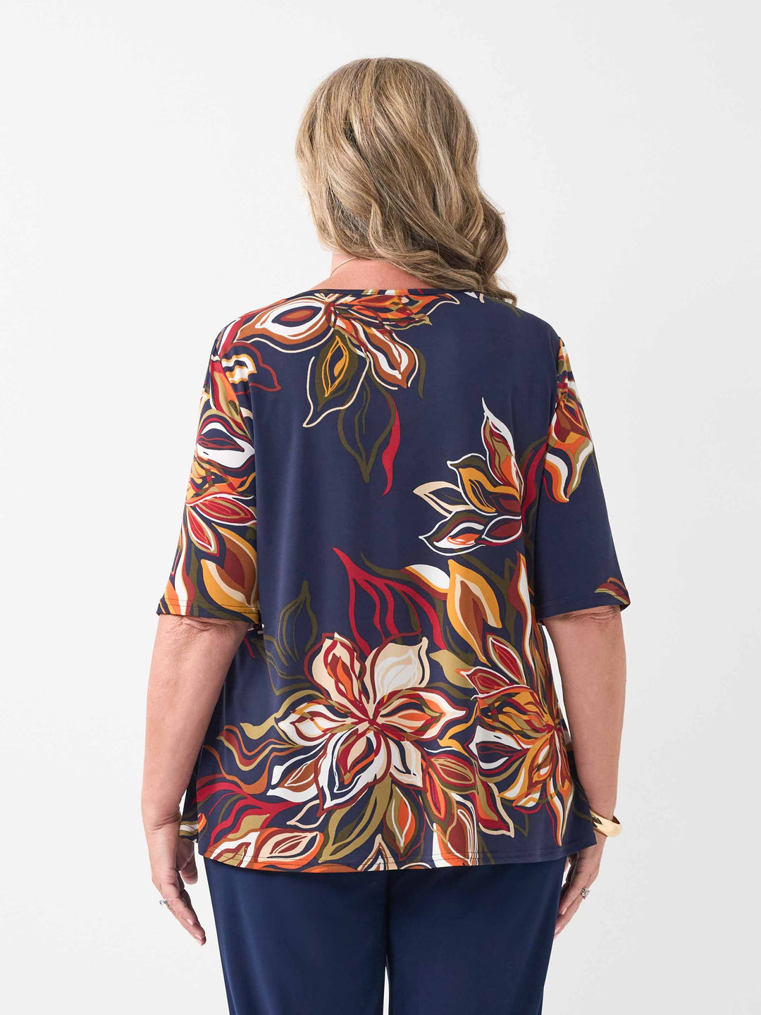 back view of model wearing a short-sleeve boat-neck top with a vibrant orange floral print on a navy blue background, paired with navy palazzo jersey pants