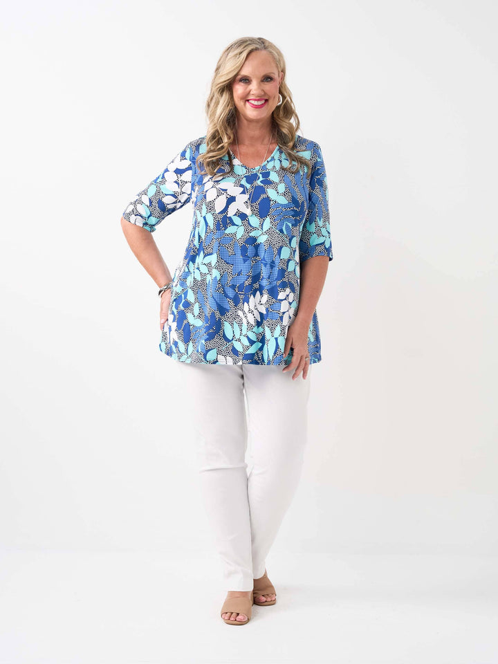 A woman wearing a blue patterned V-neck swing top with three-quarter sleeves, paired with white pants